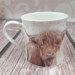 Kubek z krową highland cattle na drewnianym blacie